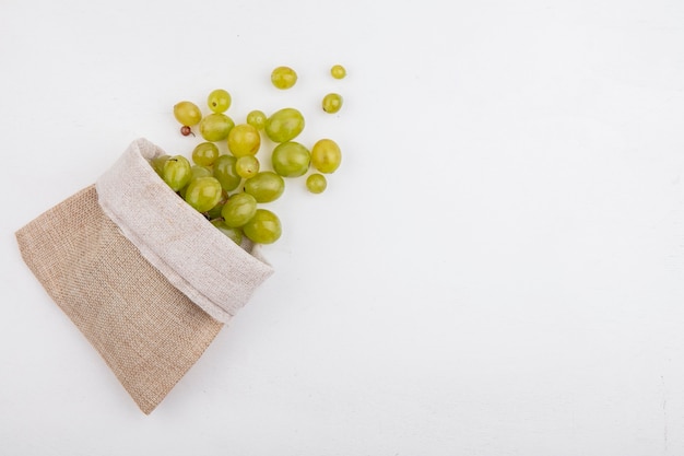 Photo gratuite vue de dessus des baies de raisin blanc s'échappant du sac sur fond blanc avec copie espace