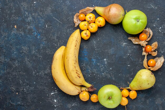 Vue de dessus bananes jaunes paire de baies avec des pommes vertes fraîches poires cerises douces sur le bureau bleu foncé baies de fruits frais santé