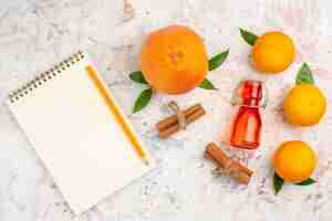 Photo gratuite vue de dessus des bâtons de cannelle mandarines fraîches bouteille orange un crayon un cahier sur une surface lumineuse