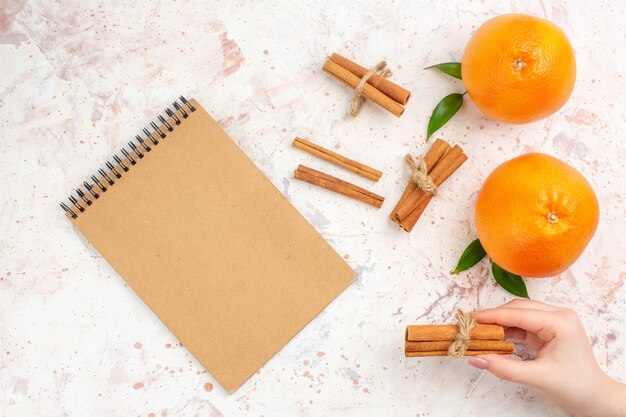 Vue de dessus des bâtons de cannelle oranges fraîches un cahier sur une surface lumineuse