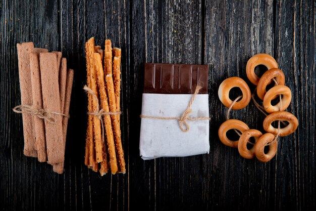 Vue de dessus des bâtons de maïs avec des baguettes de pain au chocolat et des bagels secs sur un fond en bois noir