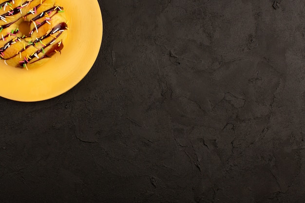 Photo gratuite vue de dessus beignet conçu avec des bonbons colorés et du chocolat à l'intérieur de la plaque orange sur le bureau sombre