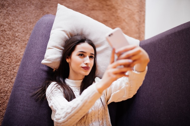 Photo gratuite vue de dessus de la belle brune prenant un selfie avec son téléphone intelligent à la maison à l'oreiller blanc