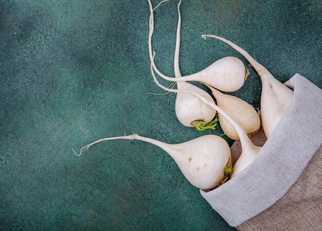 Vue de dessus des betteraves légumes racines blanches fraîches sur un sac en toile de jute sur fond vert avec espace de copie