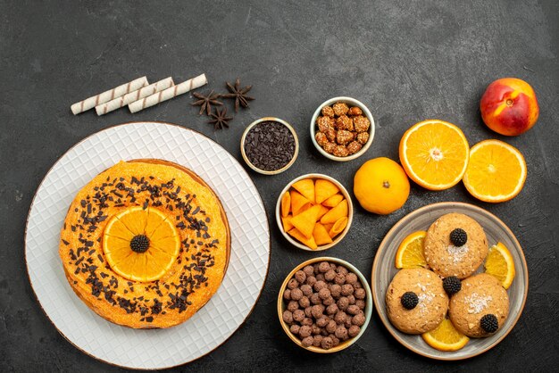 Vue de dessus des biscuits au sable avec des tranches d'orange et une délicieuse tarte sur une surface grise, un biscuit aux fruits, un thé sucré