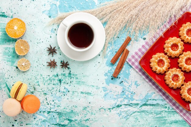 Vue de dessus biscuits au sucre à l'intérieur de la plaque rouge avec tasse de thé et macarons sur fond bleu