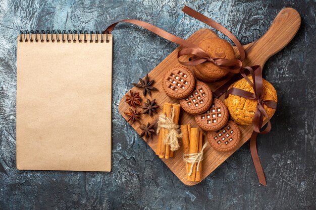 Vue de dessus des biscuits et des biscuits anis bâtons de cannelle sur le bloc-notes de service en bois sur table sombre