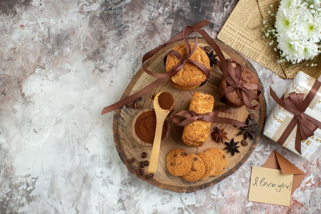 Vue de dessus des biscuits liés au cacao dans un bol sur une planche de bois, une lettre d'amour de bouquet de fleurs sur une table