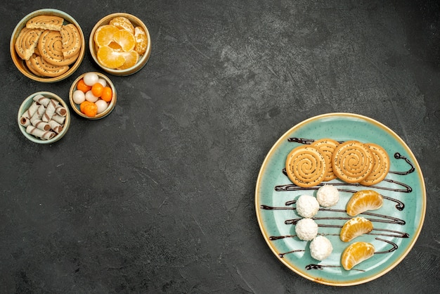 Vue de dessus des biscuits sucrés avec des bonbons à la noix de coco et des fruits sur un bureau gris foncé