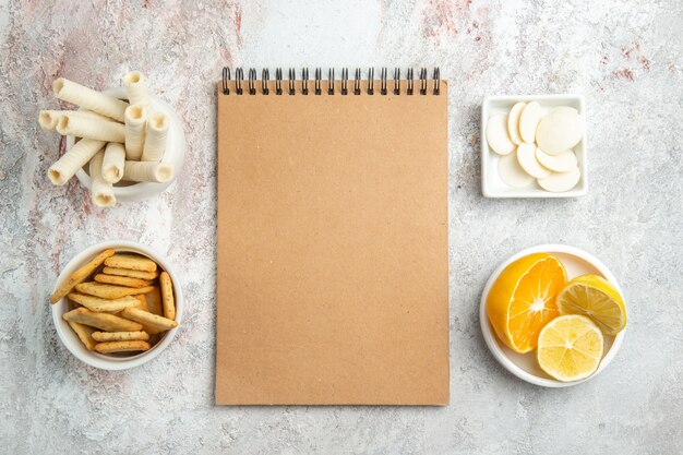 Vue de dessus des biscuits sucrés avec des craquelins et bloc-notes sur la table blanche bonbons biscuits