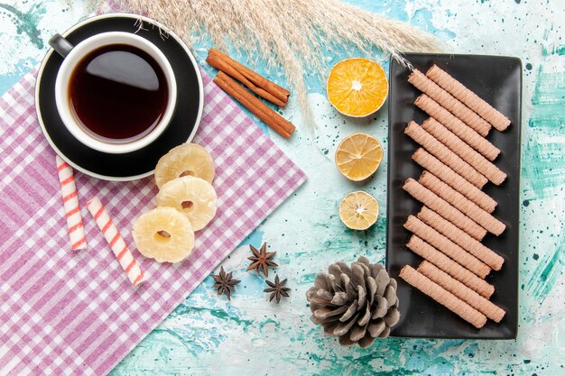 Vue de dessus des biscuits sucrés avec une tasse de thé et des anneaux d'ananas séchés sur fond bleu