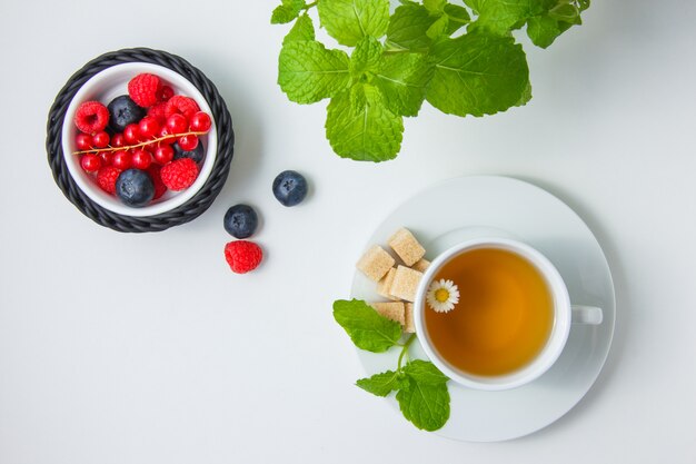 Vue de dessus bleuets et framboises dans un bol avec groseille, thé à la camomille, sucre, feuilles de menthe.