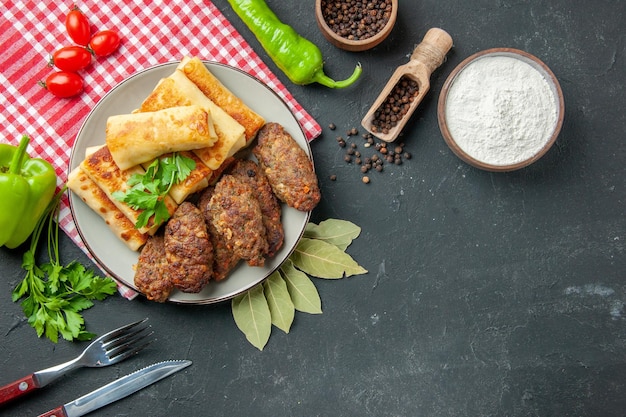 Vue de dessus blinis farcis à la viande et escalopes sur assiette ronde fourchette et couteau farine dans un bol poivrons sur table