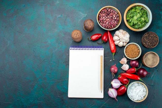 Photo gratuite vue de dessus bloc-notes blanc avec des légumes et des assaisonnements sur la photo de légume de repas de nourriture de bureau sombre