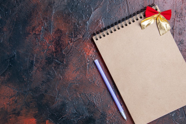 Vue de dessus d'un bloc-notes avec un petit stylo violet à arc sur une table rouge foncé avec lieu de copie