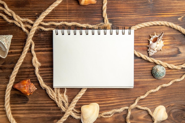 Vue de dessus bloc-notes vide avec des cordes et des coquilles sur un bureau marron