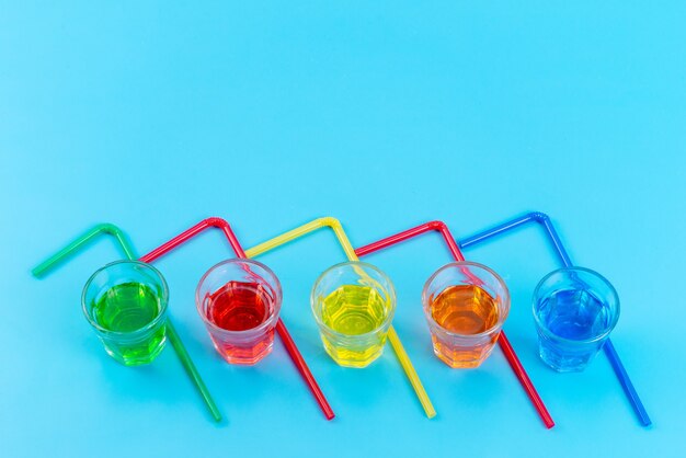 Une vue de dessus des boissons colorées à l'intérieur de verres en plastique avec des pailles multicolores isolated on blue