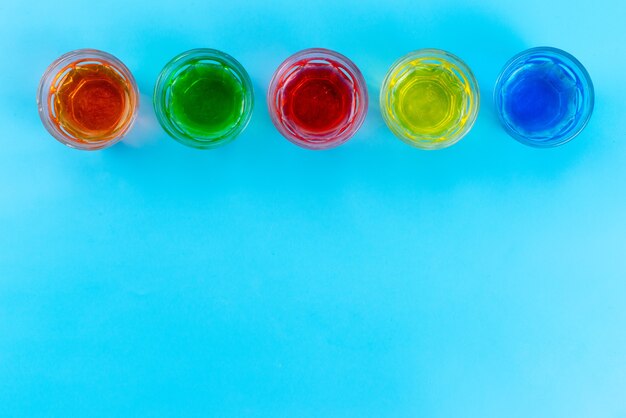 Une vue de dessus des boissons colorées à l'intérieur de verres transparents sur bleu, boire du jus de fruits couleur