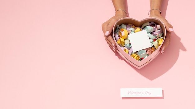 Vue de dessus de la boîte en fer blanc en forme de coeur avec des confettis pour la saint valentin et les mains de la femme