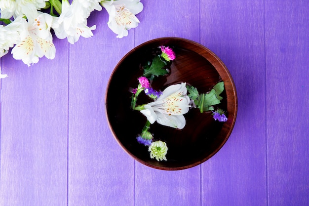 Photo gratuite vue de dessus d'un bol en bois rempli d'eau et de fleurs d'alstroemeria de couleur blanche avec statice sur fond de bois violet