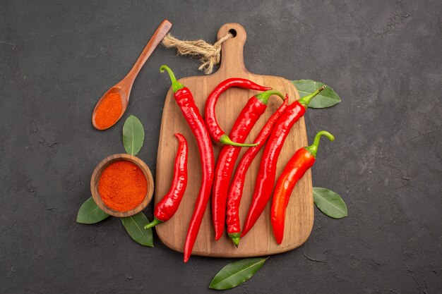 Vue de dessus un bol de poivrons rouges en poudre de piment fort sur la planche à découper les feuilles de laurier et une cuillère en bois sur la table noire