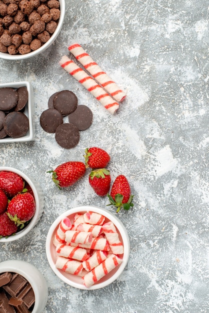 Vue de dessus des bols avec des bonbons fraises chocolats céréales bonbons et quelques fraises bonbons chocolats sur le côté gauche du sol gris-blanc