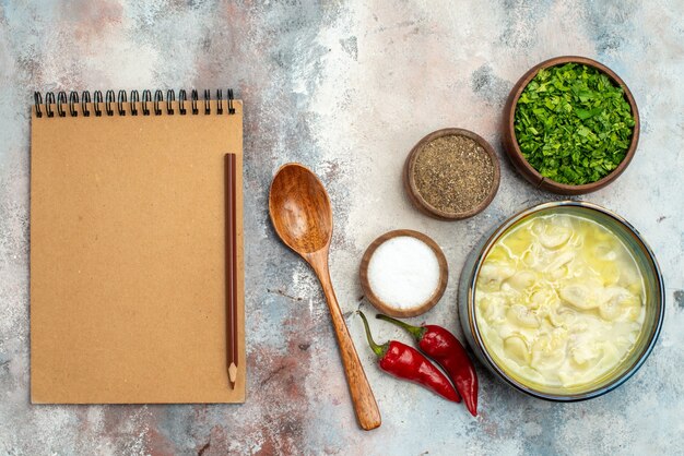 Vue de dessus bols de dushbara avec différentes épices verts cuillère en bois un crayon de cahier sur une surface nue