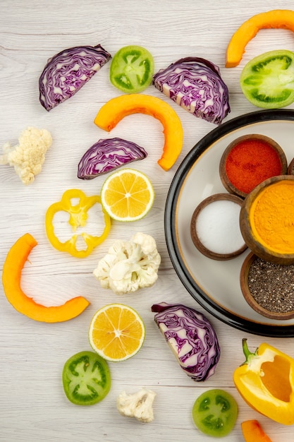 Vue de dessus des bols avec des épices sur une assiette ronde couper les légumes sur une surface blanche