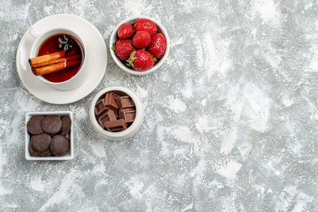 Vue de dessus des bols avec des fraises et des chocolats et du thé aux graines d'anis cannelle en haut à gauche du sol gris-blanc