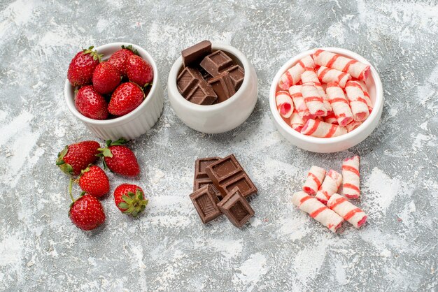 Vue de dessus des bols de rangées horizontales avec des bonbons chocolats fraises et quelques bonbons chocolats fraises le sol en mosaïque gris-blanc