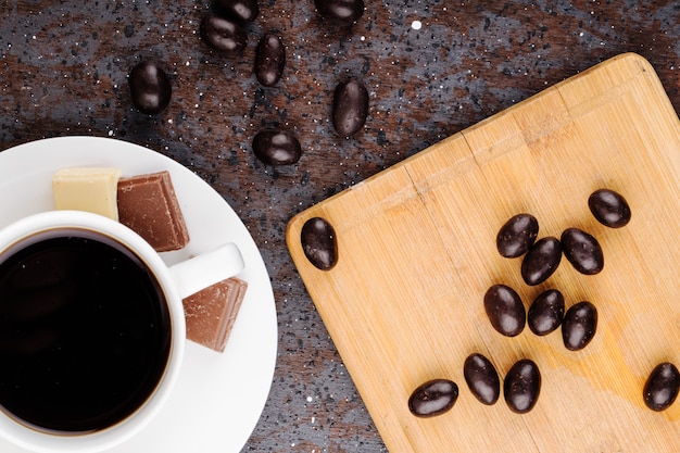 Vue De Dessus De Bonbons Aux Noix Glacées Au Chocolat éparpillés Sur Une Planche De Bois Et Une Tasse De Café Sur Fond Noir