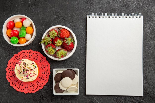 Vue de dessus des bonbons colorés avec des biscuits et des fraises sur fond sombre