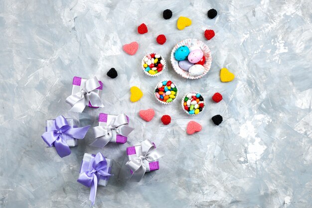 Une Vue De Dessus Des Bonbons Colorés Avec Des Marmelades En Forme De Coeur Petits Coffrets Cadeaux Violets Arcs Sur Le Fond Gris Présent Célébration Candy