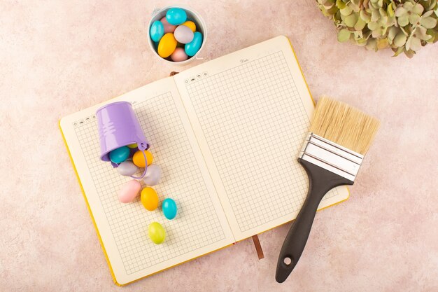 Une vue de dessus des bonbons colorés avec pinceau et cahier sur le bureau rose candy sweet sucre couleur