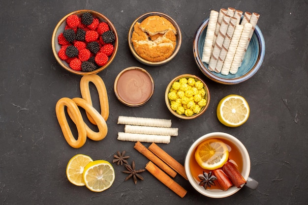 Photo gratuite vue de dessus des bonbons à la confiture avec une tasse de thé et des biscuits sur une surface sombre thé aux biscuits aux bonbons sucrés