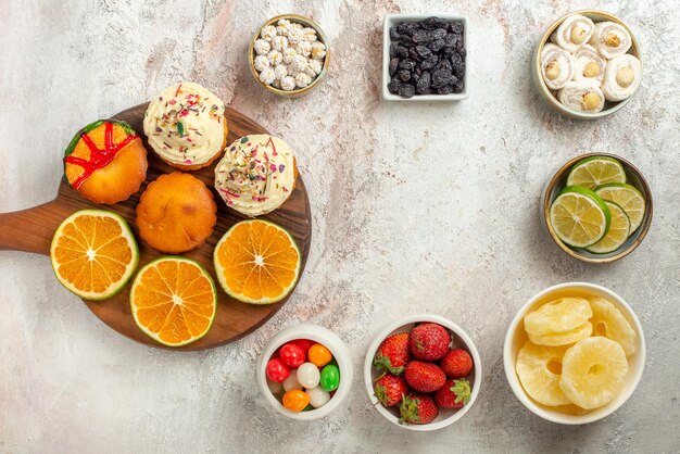 Vue de dessus des bonbons dans des bols en bois avec des biscuits et de l'orange à côté des fraises au citron de l'ananas séché et des délices turcs dans des bols sur la table