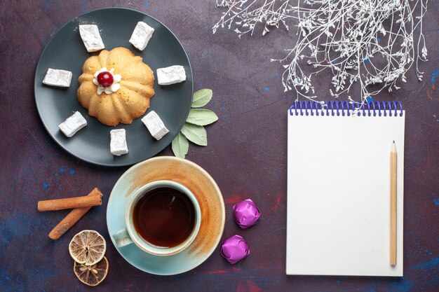 Vue de dessus des bonbons en poudre de sucre délicieux nougat avec gâteau et tasse de thé à l'intérieur de la plaque sur une surface sombre