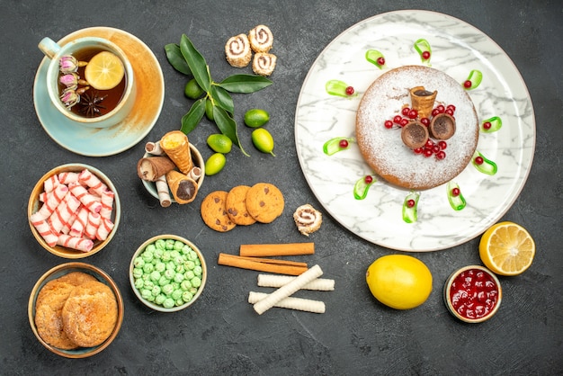 Vue de dessus des bonbons une tasse de tisane un gâteau aux baies biscuits gaufres bonbons confiture citrons