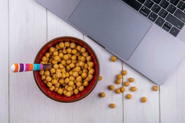 Vue de dessus des boules de maïs dans un bol avec un ordinateur portable sur une surface blanche