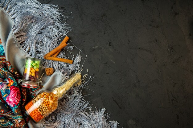 Vue de dessus d'une bouteille avec des graines de maïs crues et des bonbons aux haricots et un bâton de cannelle sur un châle avec un gland avec copie espace sur fond noir