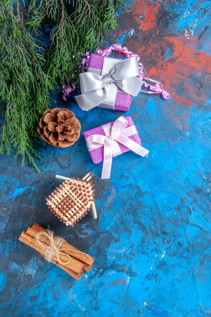 Vue de dessus branches de pin jouets d'arbre de noël cadeaux de noël bâtons de cannelle sur une surface bleu-rouge