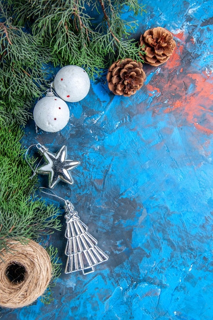 Photo gratuite vue de dessus branches de pin pommes de pin boules d'arbre de noël fil de paille sur une surface bleu-rouge