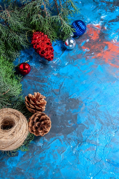 Photo gratuite vue de dessus des branches de pin avec des pommes de pin et des jouets d'arbre de noël colorés fil de paille sur une surface bleu-rouge