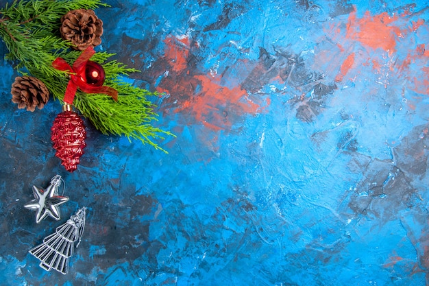 Vue de dessus des branches de pin avec des pommes de pin, des ornements suspendus rouges et argentés sur une surface bleu-rouge