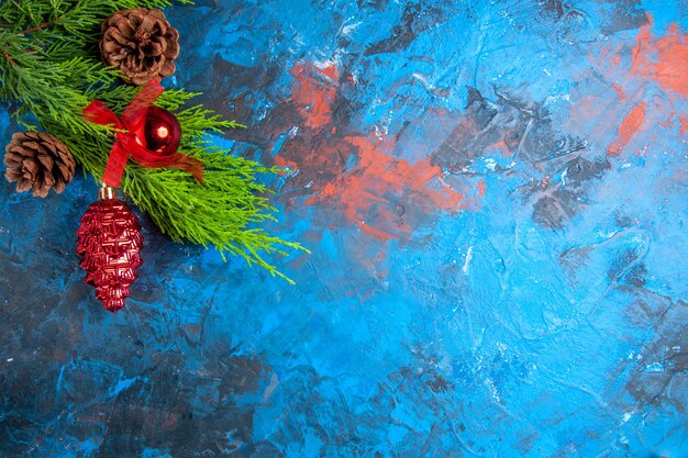 Vue de dessus des branches de pin avec des pommes de pin et des ornements suspendus sur une surface bleu-rouge