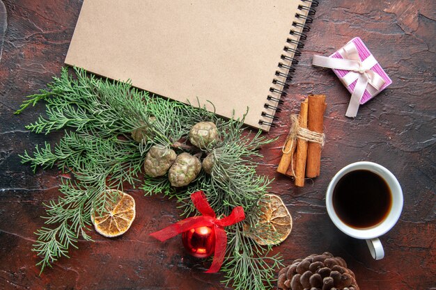 Vue de dessus des branches de sapin et cahier à spirale fermé avec stylo citrons cannelle cadeau une tasse de thé noir sur fond sombre