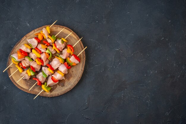 Vue de dessus de la brochette de poulet cru sur une planche de bois sur un espace libre de table sombre