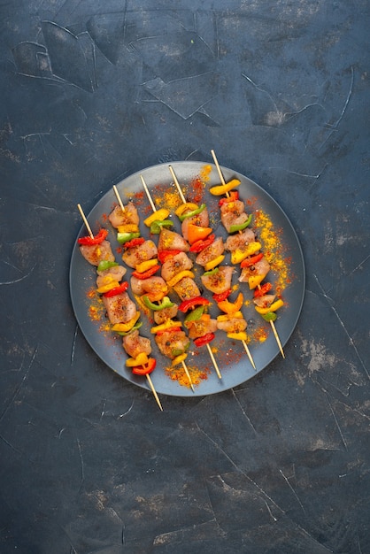 Vue de dessus des brochettes de poulet cru aux épices sur planche de bois sur table noire avec copie place