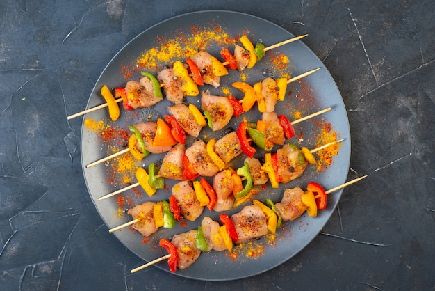 Vue de dessus des brochettes de poulet cru aux épices sur planche de bois sur table sombre