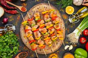 Photo gratuite vue de dessus des brochettes de poulet cru sur une planche de bois naturel et d'autres trucs sur une table sombre